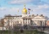 Capitol building with golden dome and several flags waving.