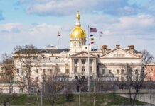 Capitol building with golden dome and several flags waving.