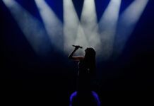 Silhouetted singer performing on stage with spotlights above.