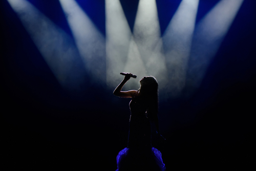 Silhouetted singer performing on stage with spotlights above.