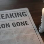 A newspaper with the headline 'BREAKING ICON GONE' next to a lit candle