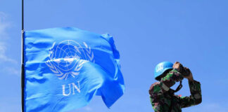 UN soldier with binoculars next to United Nations flag.