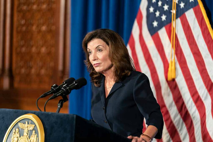Woman speaking at podium with American flag backdrop.