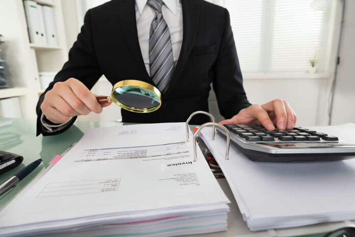 Person examining documents with magnifying glass and calculator.