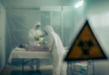 Two scientists examining a patient with biohazard sign visible.