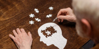 Elderly person assembling a head-shaped jigsaw puzzle on a wooden table