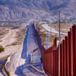 Border wall stretching through desert landscape with mountains.