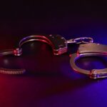 A pair of metallic handcuffs on a dark background with red and blue lighting