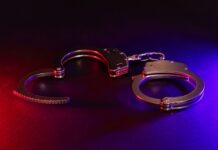 Police Chief Under FIRE — Unthinkable BETRAYAL A pair of metallic handcuffs on a dark background with red and blue lighting