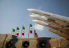 Iran Admits Crisis, Plots Crackdowns Missiles on launchers beside Iranian flags.