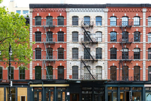 shutterstock_1033775263 Red-brick building with fire escapes and storefronts, daytime.